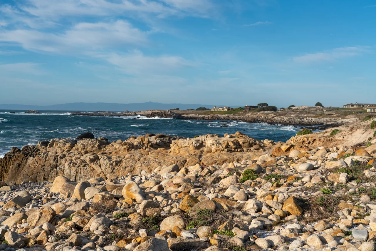 Golden rocks along a blue coastline beneath scattered clouds.